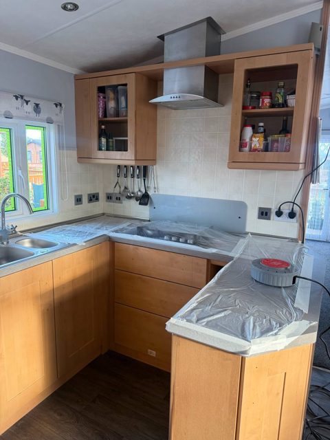 Caravan kitchen with orange wood-effect units and glass-fronted wall cupboards, before